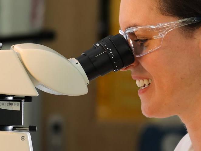 Woman wearing safety goggles looking through a biology microscope