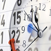 A close-up image of a calendar with a clock superimposed on it. The calendar shows dates 14, 15, 22, and 23. A red push pin is stuck into the calendar on the 22nd. The clock hands are pointing at 12:00.