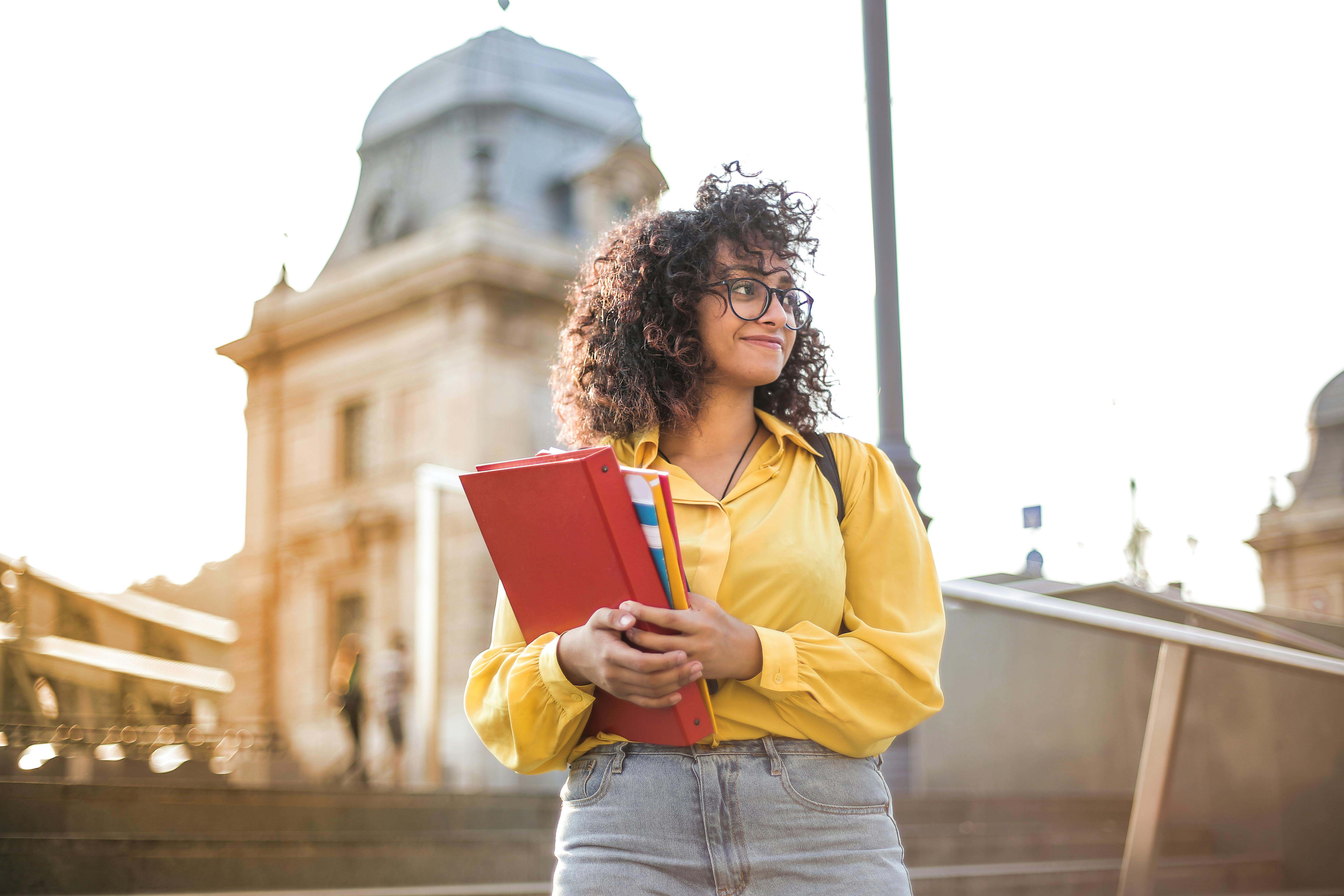 female student holding books in front of a building