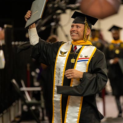 ksu navy student at graduation holding their diploma up in excitement.