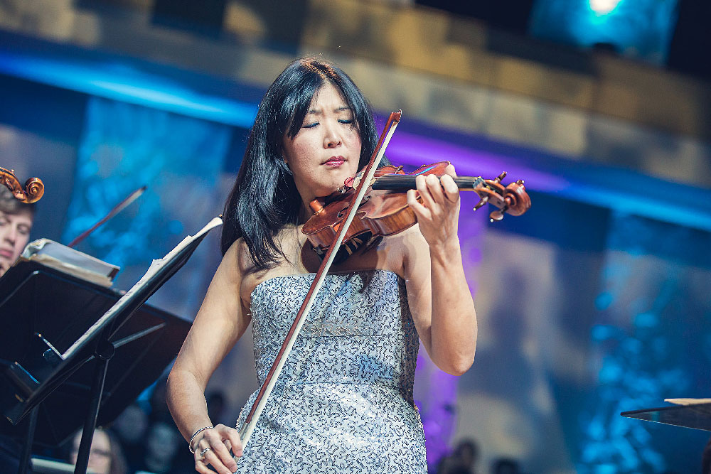 KSU professor of violin Helen Kim playing the violin on stage in a silver blue dress