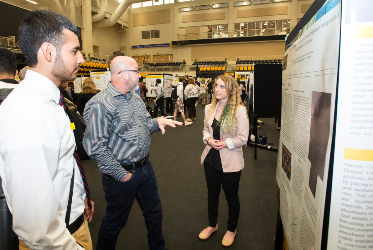 3 students standing by a presentation poster