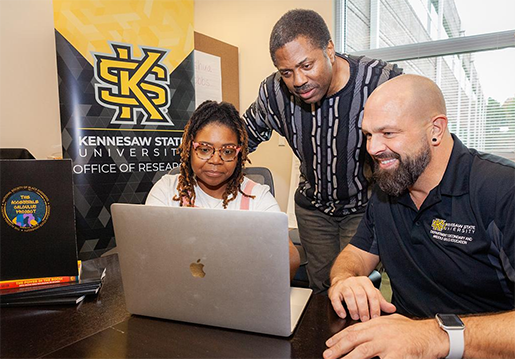 Picture of Dr. Alan Shaw, Dr. Brian Lawler, and Prof. Deepa Muralidhar around a laptop