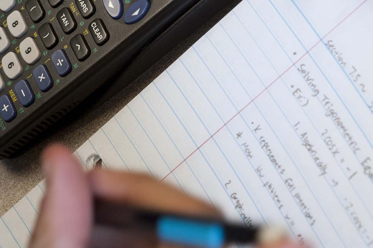 Student writing mathematics equations on paper using a calculator.  / Student writing mathematics equations on paper using a calculator. 