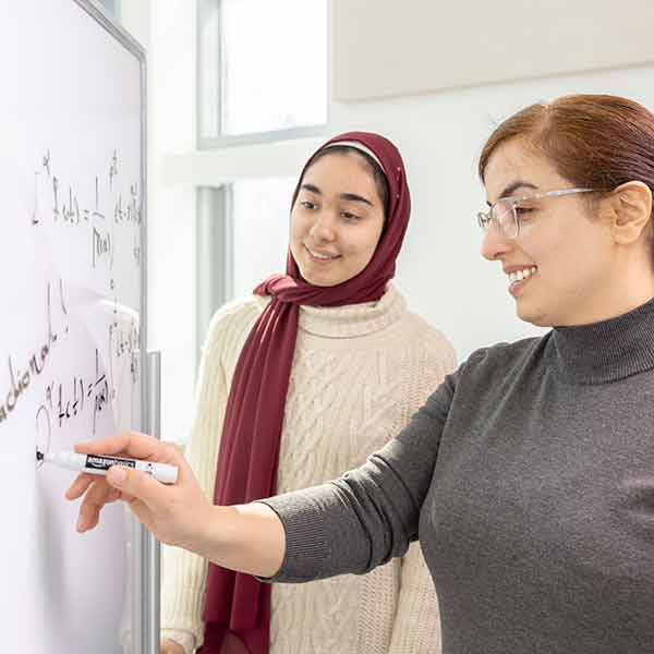 Mathematics faculty and student writing a math problem on a white board