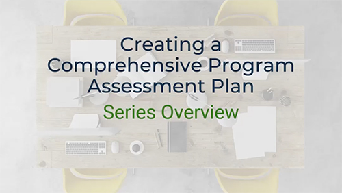 A top-down view of a conference table with a laptop, keyboard, mouse, pens, and papers scattered across it. The text "Creating a Comprehensive Program Assessment Plan" and "Series Overview" is written on the table. Two yellow chairs are visible on either side of the table.