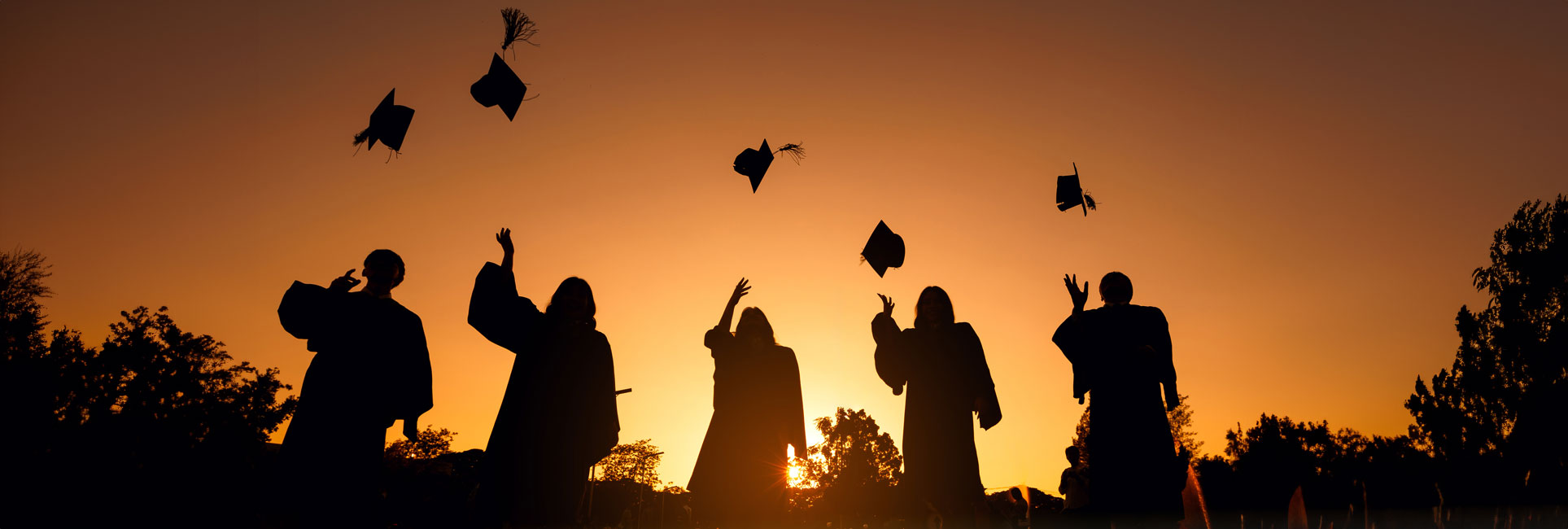 Silhouettes of KSU graduates in caps and gowns celebrating at sunset, throwing their graduation caps into the air, symbolizing achievement and the completion of their academic journey.