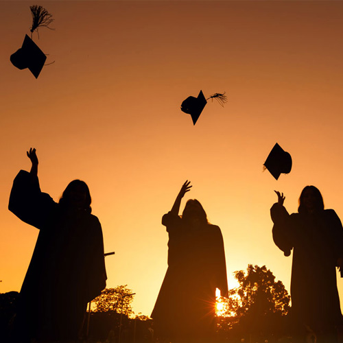 Silhouettes of KSU graduates in caps and gowns celebrating at sunset, throwing their graduation caps into the air