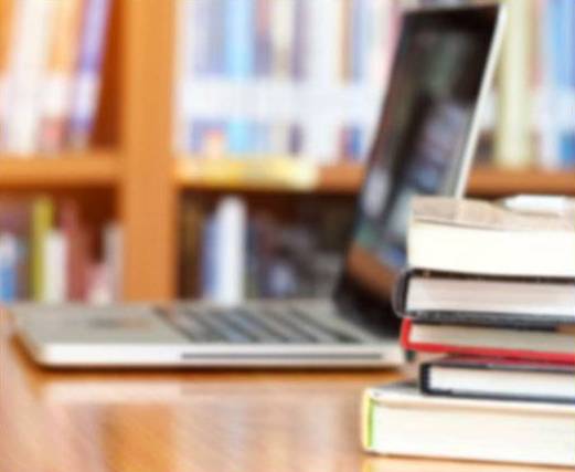 a laptop and stack of books sitting on a table in the library.