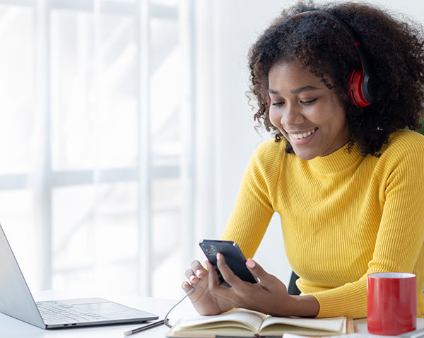 Woman with headphones on in gold sweater engaged with other students on her phone