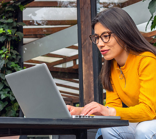 Women in gold sweater working on laptop outside