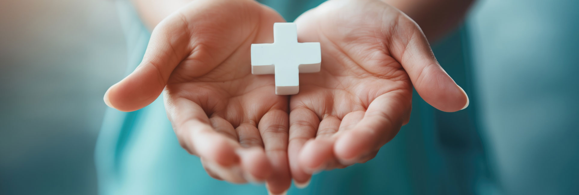 A pair of open hands holding a small white cross.