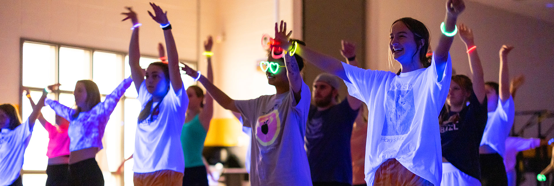 A group of employee well-being champions standing in a line, smiling and with arms outstretched in a welcoming, open gesture as they engage in after work Zumba Glow class.