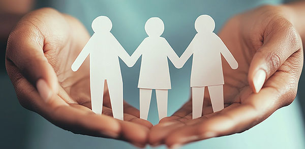 Close-up of hands gently holding three cutout paper figures of people, symbolizing support, community, and well-being.