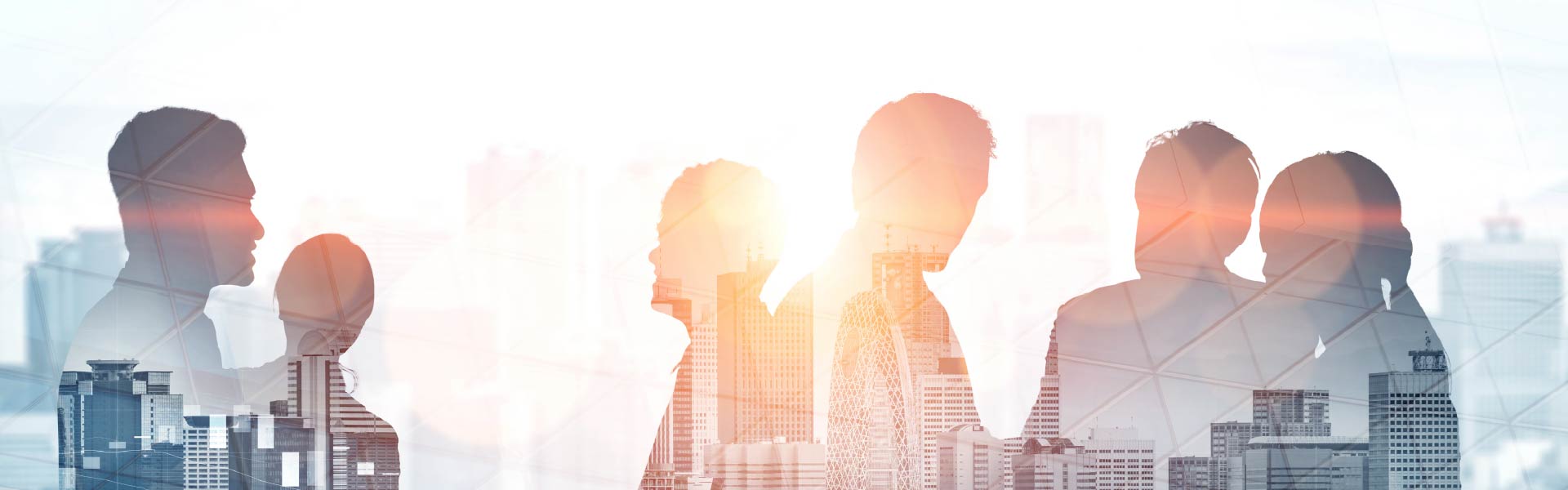Shadows of business men and women in front of a window with a sunrise and city scape behind them