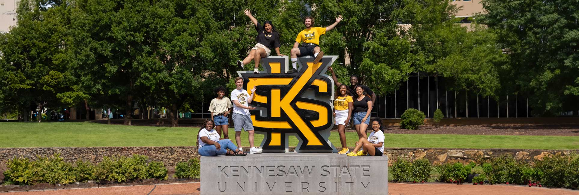 A group of Kennesaw State University students standing on the university's logo, posing for a photo.