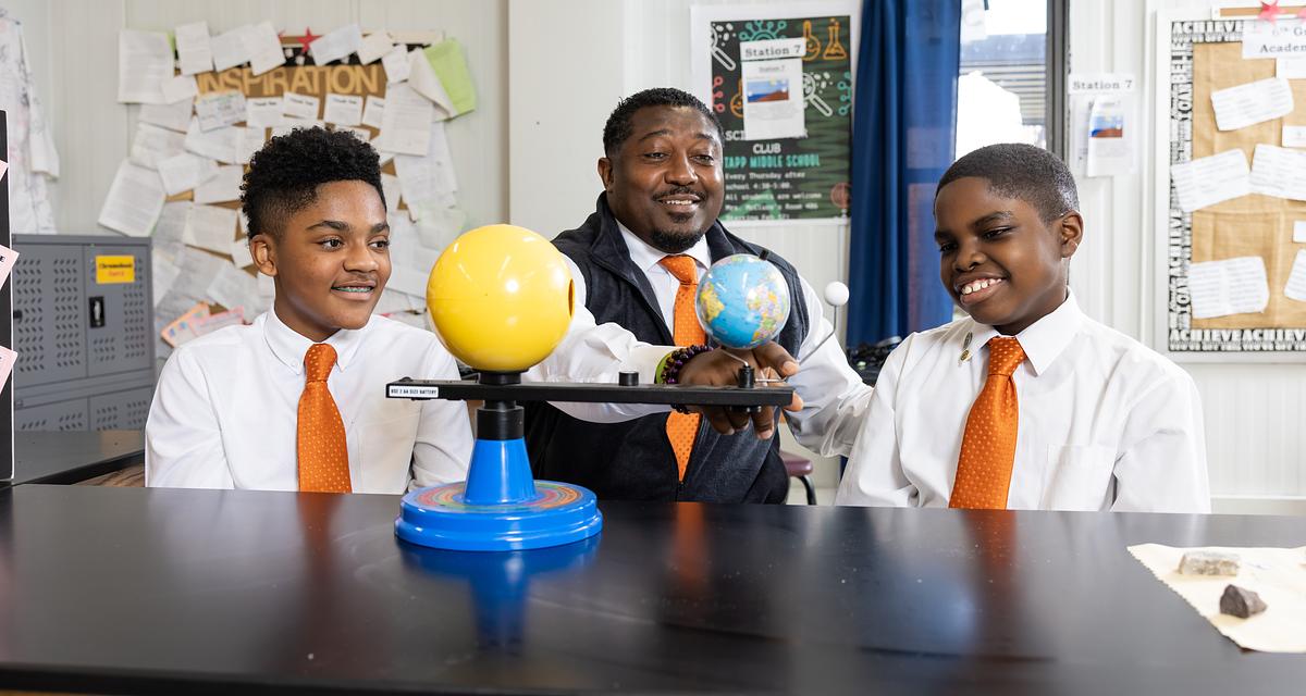 a teacher uses models to explain the position of the sun, earth and moon to two students.