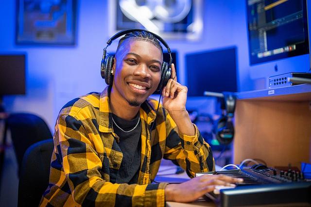 A male student sits by recording equipment with headphones on