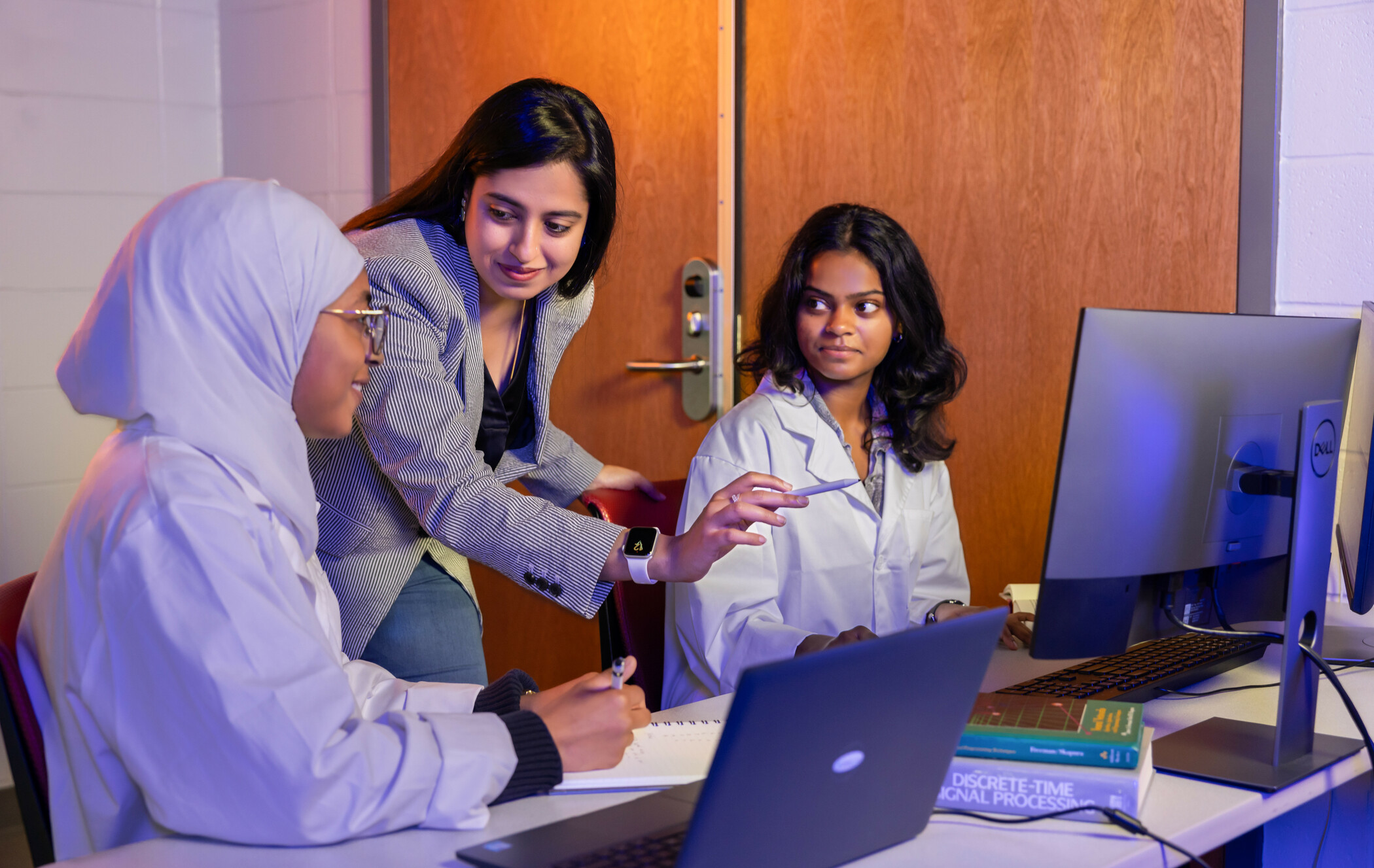 Two female students collaborate with a female research faculty member by a computer on a project