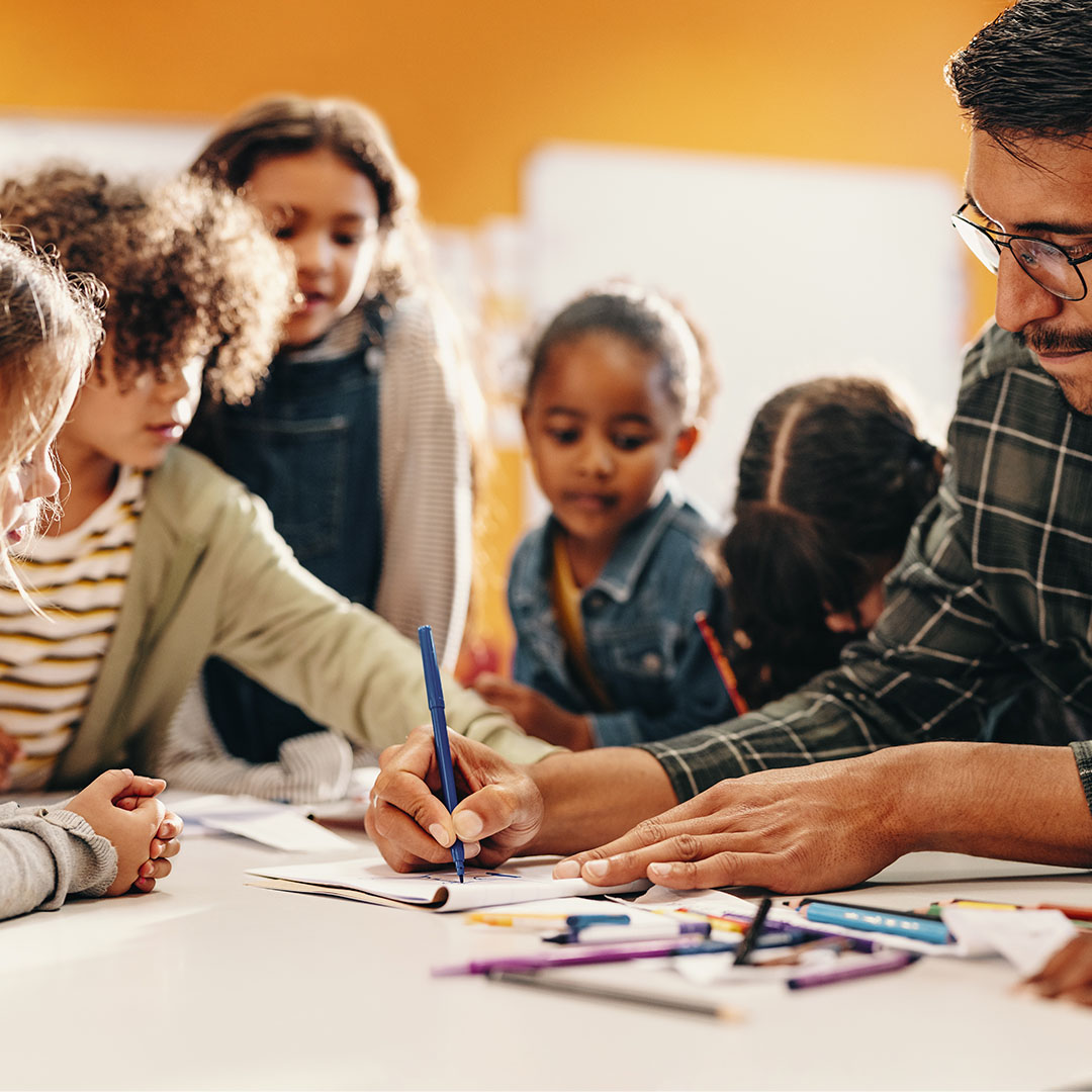 A teacher guiding a group of young students through a hands‑on art activity at a table covered with drawing supplies.