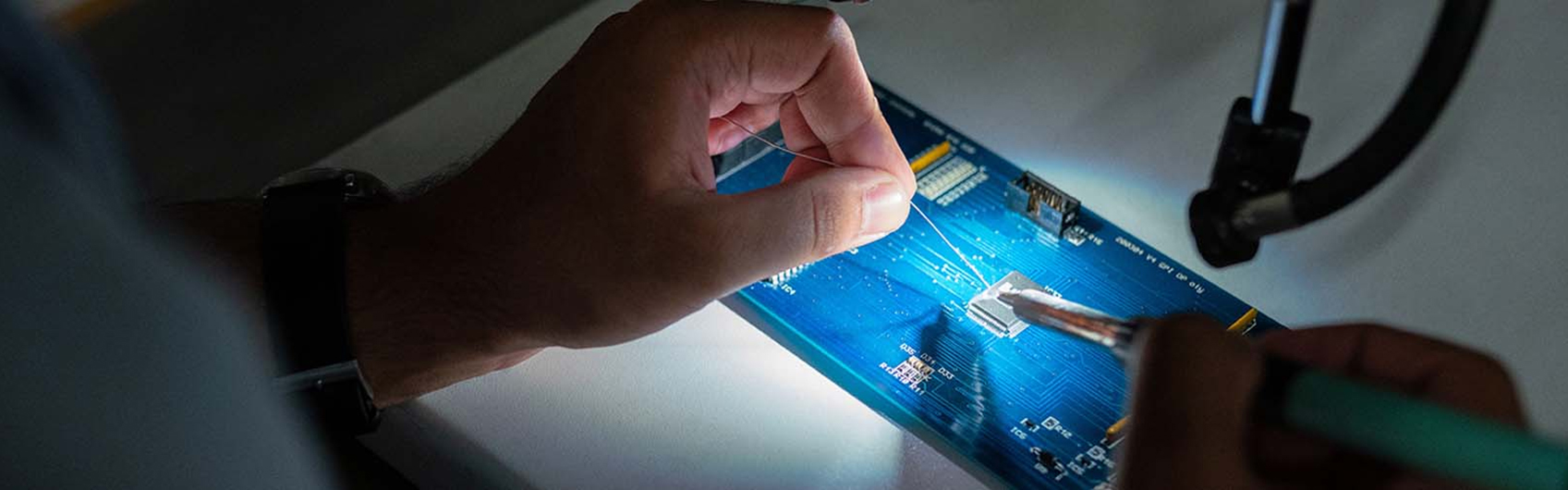 A person soldering an electrical wire onto a computer motherboard.