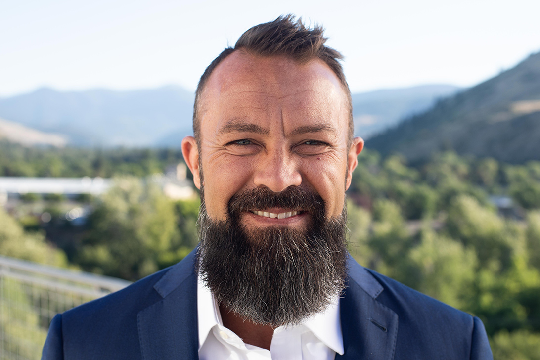 caucasian male graduate student smiling in suit and tie outside front of blue skies