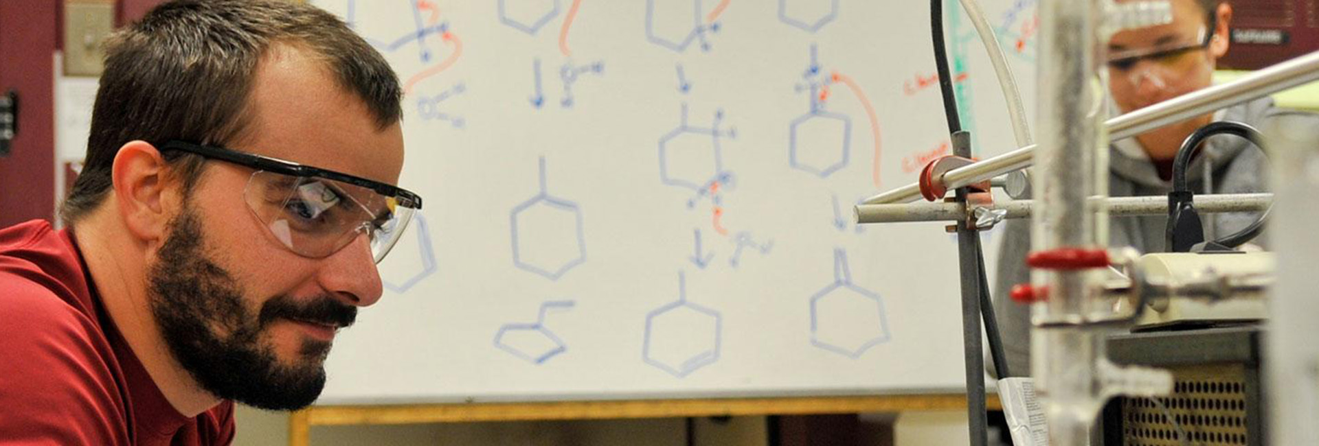 man in lab goggles with a woman in lab goggles white board in background