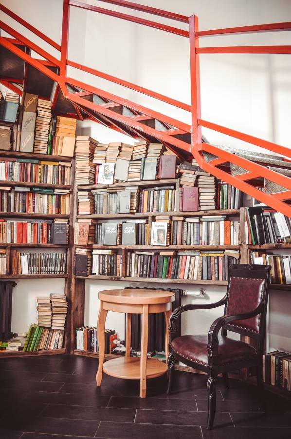 books on a shelf under a circle of stairs.