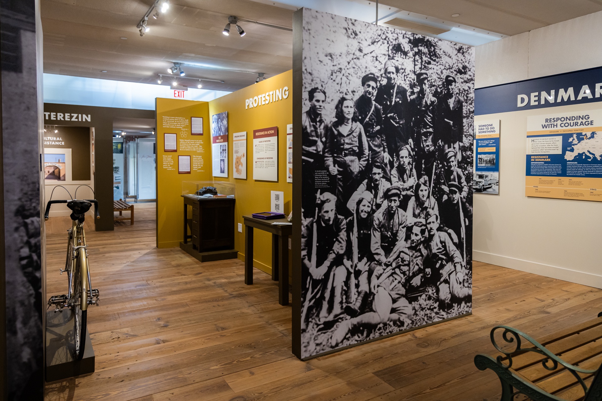 A potion of the Save One Life exhibit showing a bicycle and several display cases, photograph panels, and informational panels on the walls.