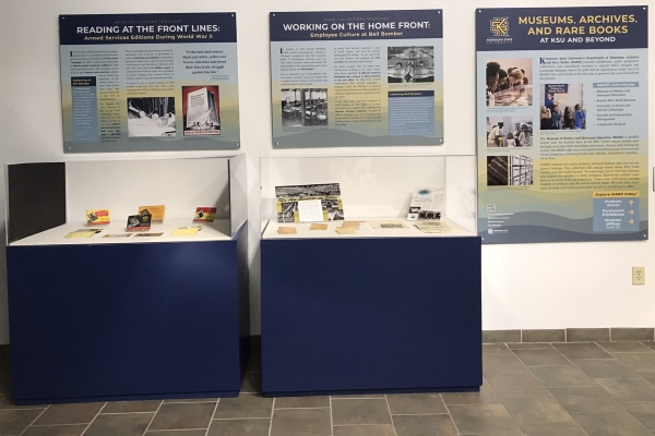 Glass display stands with artifacts related to World War II and th Holocaust. Above the cases are 3 exhibition signs.