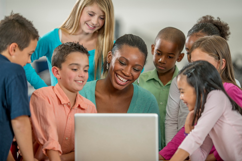 teacher and students around a laptop