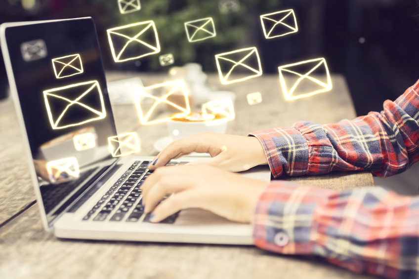 email icons floating above hands typing on a laptop keyboard