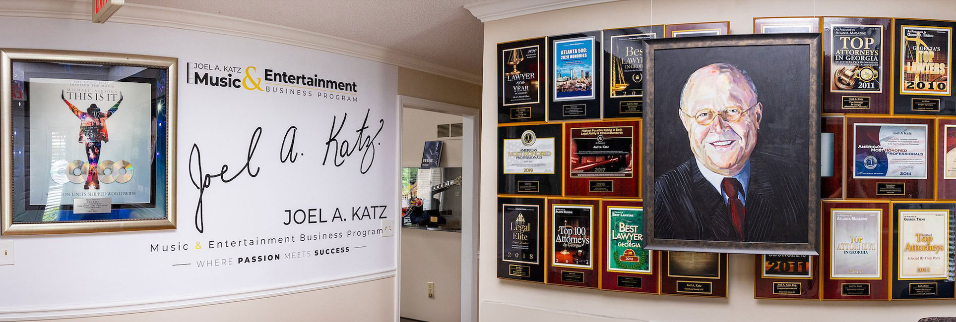 The image showcases a framed poster for Michael Jackson's This Is It. There's a wall filled with numerous plaques and awards, recognizing achievements and accolades. Adjacent to this is branding for the "Joel A. Katz Music & Entertainment Business Program,This setting emphasizes professional accomplishments and educational excellence.