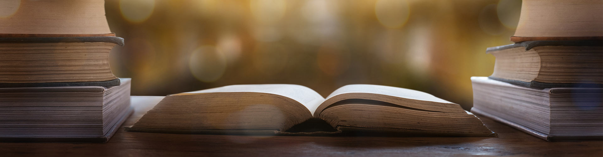 An open book with aged pages resting on a wooden table, surrounded by closed books.