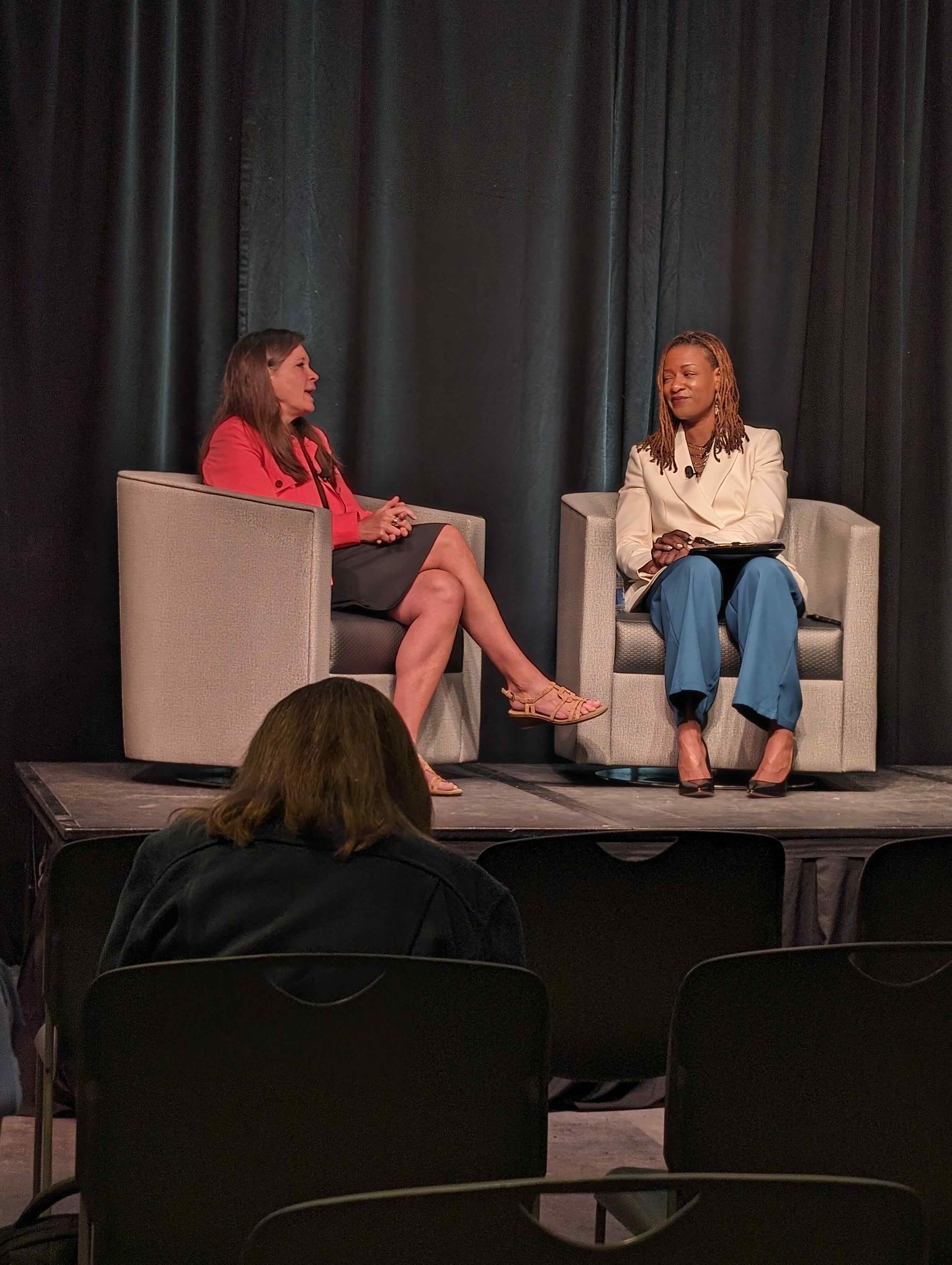 two women talking seated on a stage