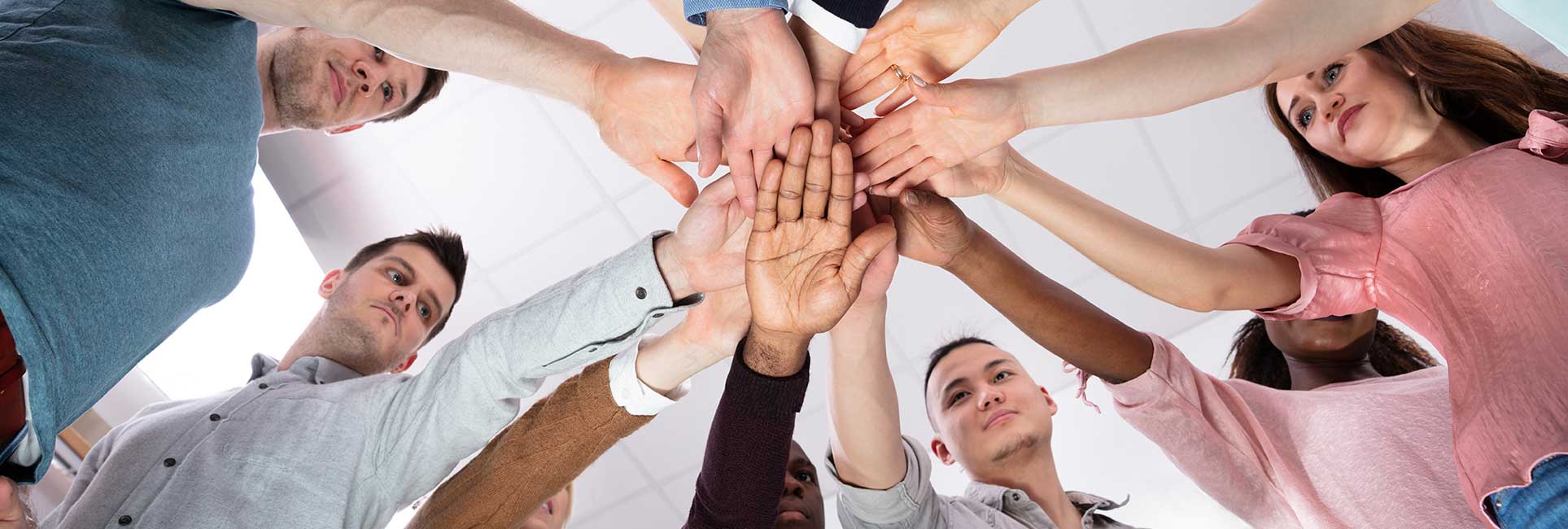 A diverse committee group standing in a circle, reaching their hands into the center to form a unified stack.