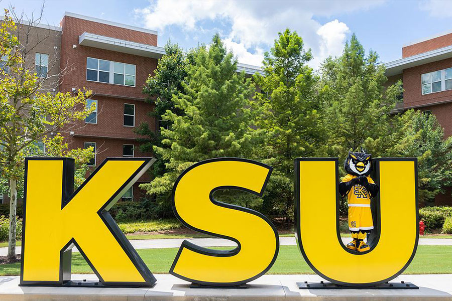 scrappy taking a picture at the ksu sign on campus.