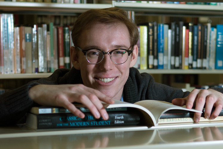 student with chin on book with an open book on desk in library