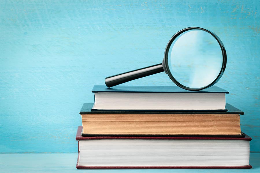 Three books with a magnify glass sitting on top of them.