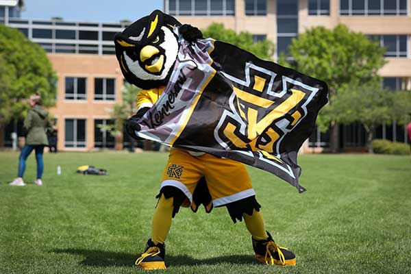 scrappy holding ksu flag on campus lawn