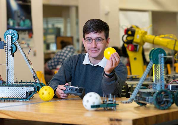 student holding ball and controller with robot arm in background