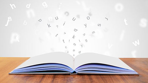 Book open on a table with letters of words floating out of it