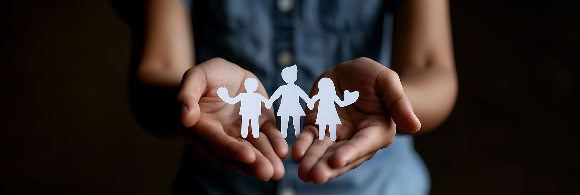 A pair of hands cupped together, holding a family of three paper cutouts.