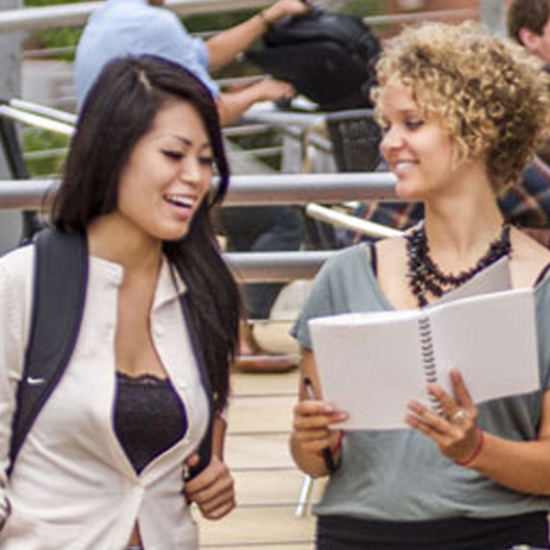 Two Department of civil and environmental engineering students standing on a bridge, engaged with a laptop, symbolizing innovation and collaboration in a scenic environment.