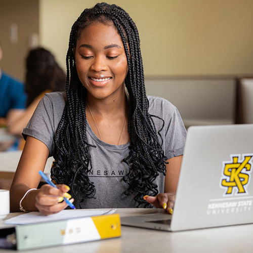 KSU Student working on laptop with KSU logo on the laptop