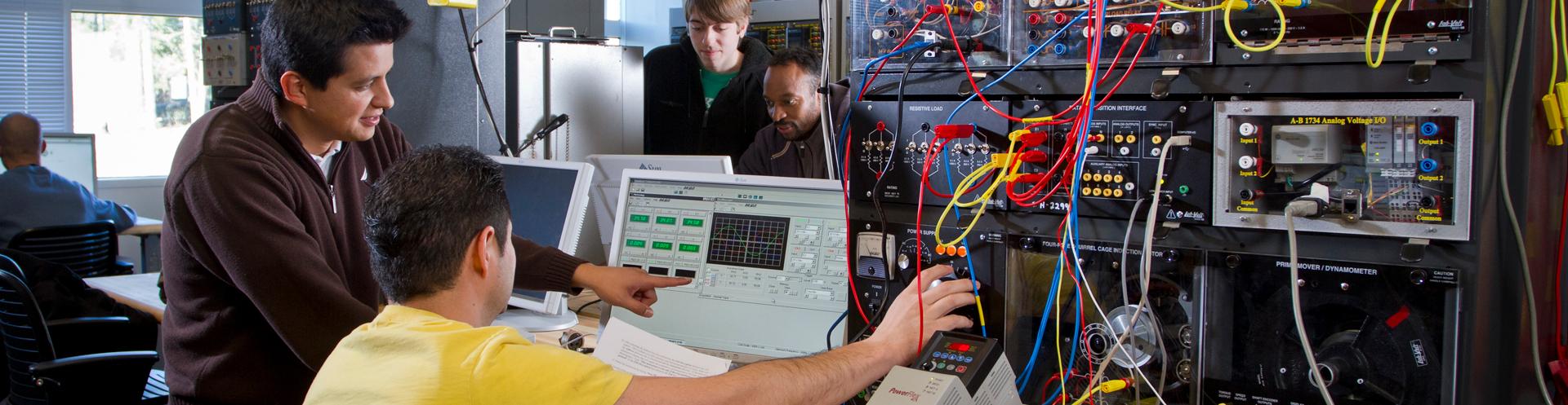 4 men one pointing at a computer one mans hand on a dial