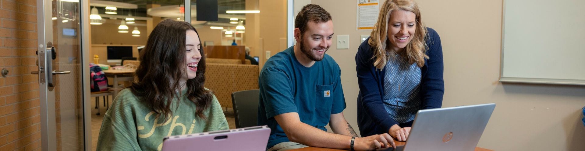 KSU students and faculty at a desk smiling and working on a laptop.