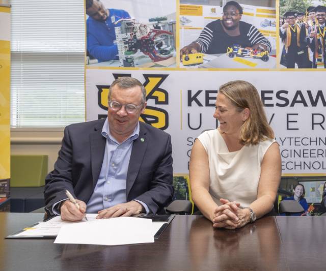 Two KSU faculty members sitting at a table, with one member signing a document