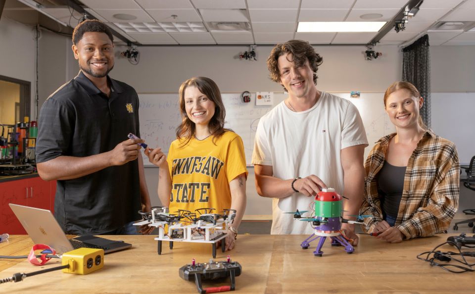 Four students at KSU, smiling and showcasing their robotic engineering project.