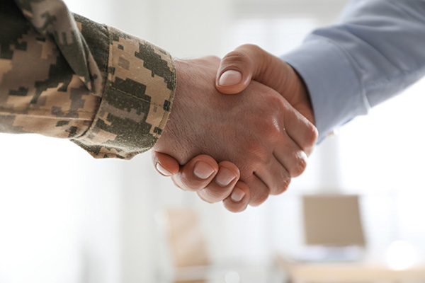 Close-up of a handshake between a person in military camouflage uniform and a person in a business suit, symbolizing partnership or collaboration.